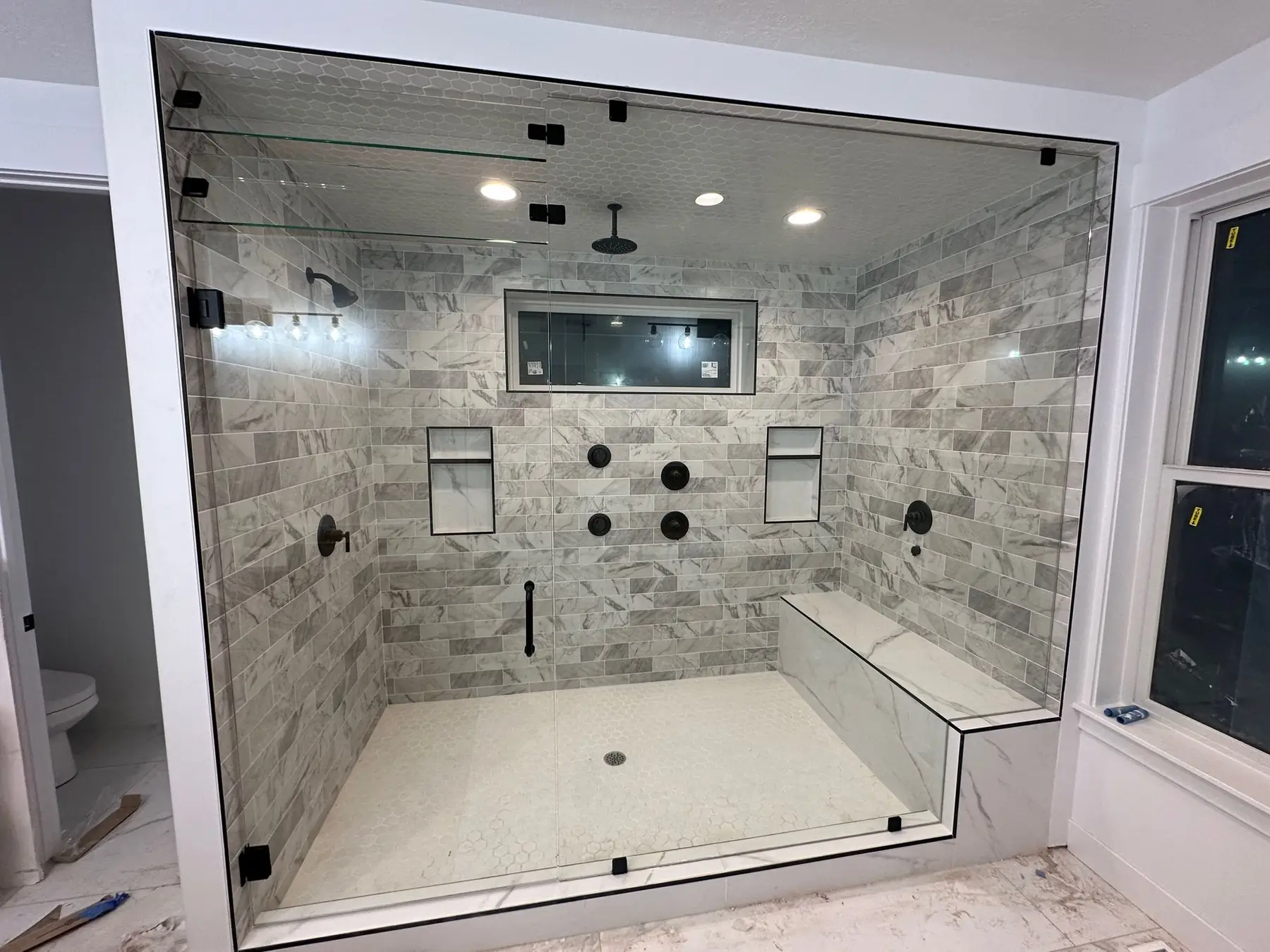 Large frameless steam shower enclosure with matte black hardware and a glass transom