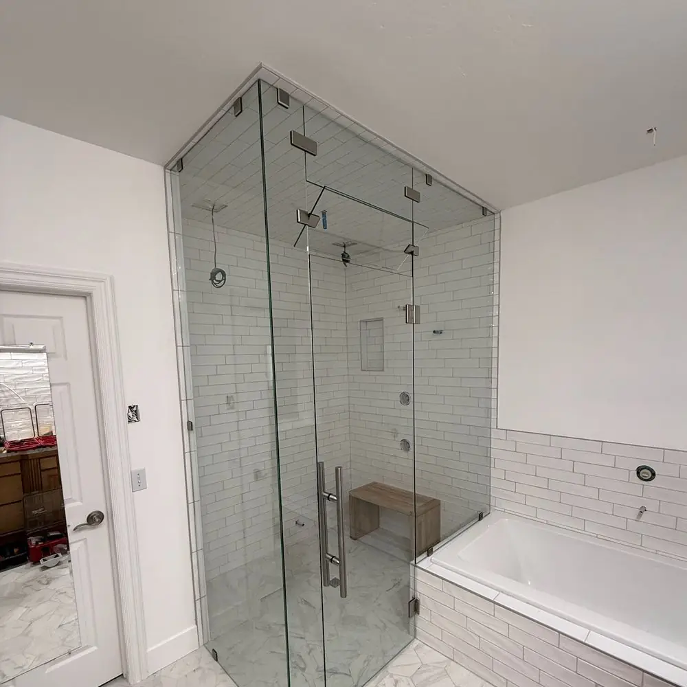 Frameless glass steam shower enclosure with brushed nickel hinges and pull handle