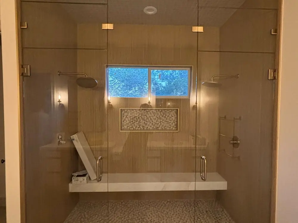 Double-door frameless steam shower with brushed hardware and a tiled bench