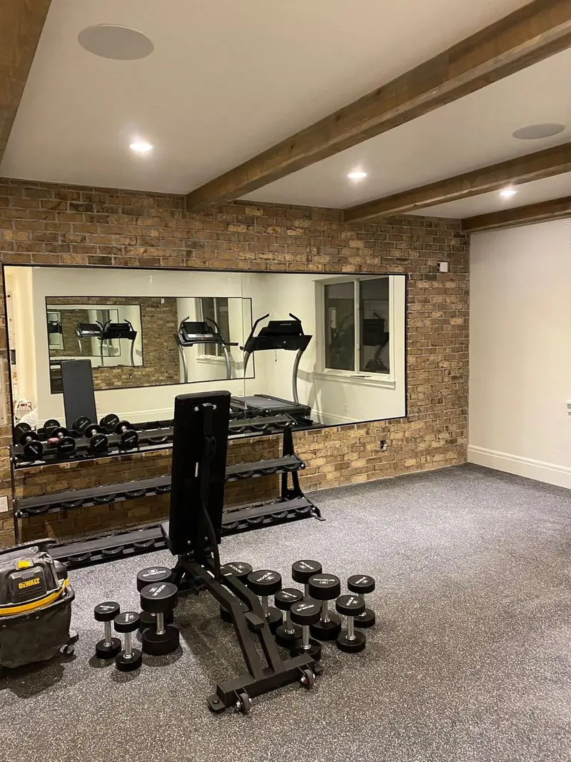 Wall-to-wall mirror installed in a home gym with a brick wall