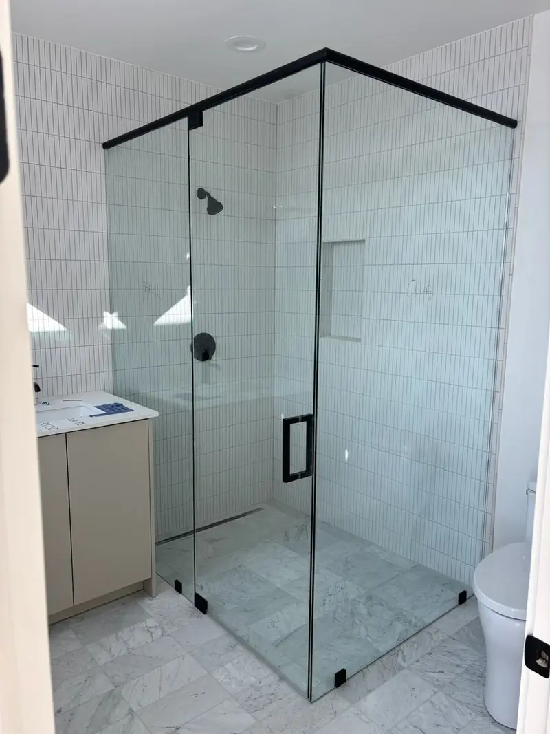Frameless corner shower enclosure with a matte black header and handle